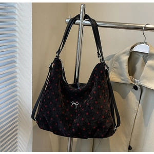 Close-up of black corduroy shoulder bag with red polka dots and silver metal bow detail
