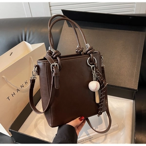 Detail of dark brown bucket bag with unique baseball charm and leather texture