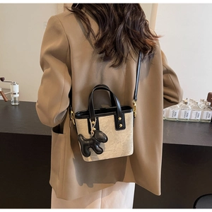Detail of a beige bucket bag with black leather trim and dog charm in a cafe setting