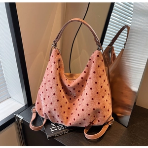 Detailed view of a pink polka dot tote bag with metal bow charm on a bookshelf