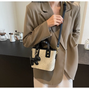 Detailed view of beige textured bucket bag with black handle and cute dog charm accessory