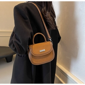 Détail d'un sac selle en cuir marron porté par un mannequin avec plaque bouclée argentée
