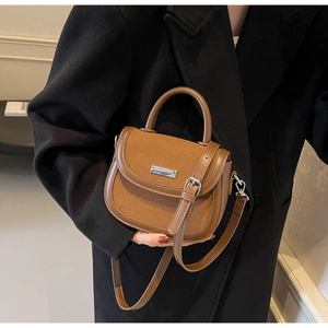 Détail d'un sac besace marron en cuir porté par un mannequin en manteau noir classique