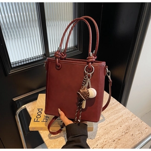 Detail view of burgundy bucket bag with smooth PU leather finish and baseball bag charm