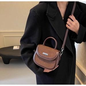Détail du sac besace marron bimatière porté par un mannequin en manteau noir