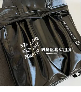 Detail of glossy black tote bag featuring white printed text and textured webbing handle
