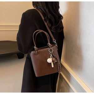 Detail of a brown bucket bag with baseball charms on a black wool coat backdrop