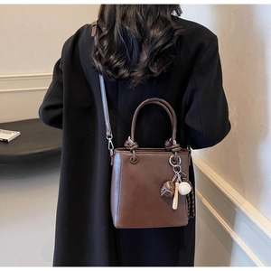 Brown leather bucket bag with baseball charms shown on a model in a black wool coat