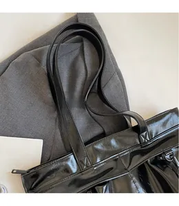 Close-up of black glossy tote bag with smooth shoulder strap and metal zipper detail