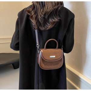 Détail du sac selle marron avec plaque métallique sur un manteau en laine noir