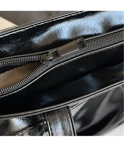 Close-up of sleek black glossy leather bag featuring high-shine metal zipper detail