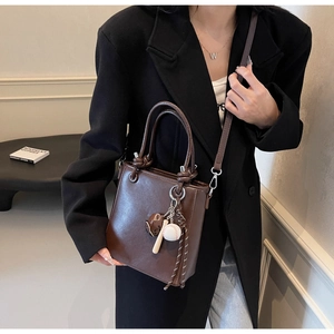 Close-up of dark coffee leather bucket bag with baseball charm and adjustable strap detail
