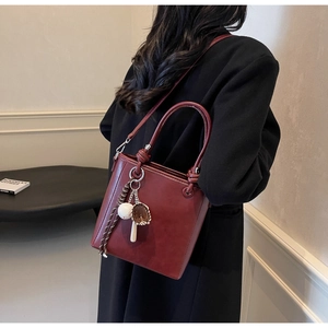 Detail of burgundy bucket bag featuring baseball charms and premium matte leather finish