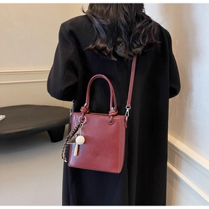Detail of dark red leather bucket bag featuring a baseball charm on black wool coat