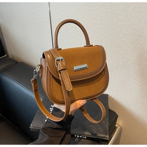 Détail du sac selle marron montrant la texture daim, le fermoir argenté et la poignée