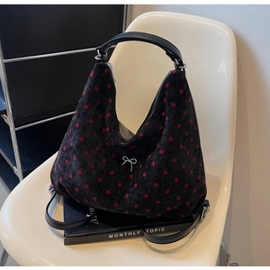 Detail of black tote bag with red polka dots and white metal bow charm on a chair
