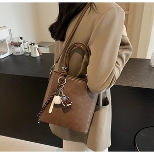 Detail view of brown leather bucket bag with creative baseball charm and shoulder strap