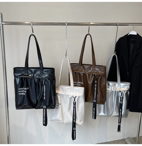 Multiple colors of large shiny PU tote bags displayed on a rack with slogan print
