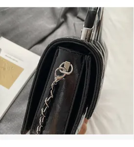 Gros plan du sac en cuir verni noir matelassé avec poignée en anneau argenté et chaîne