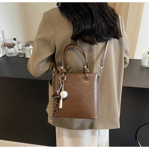 Detail of dark brown leather bucket bag with baseball charms on a cafe background