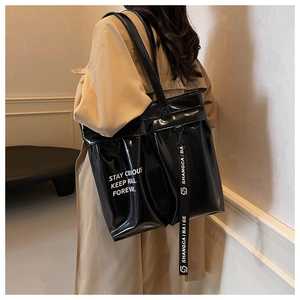 Detailed close-up of glossy black tote bag with white slogan and decorative logo strap