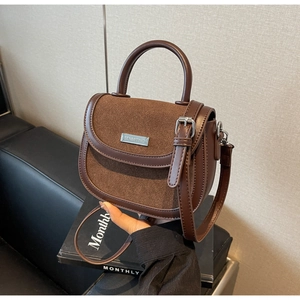 Détail du sac selle marron foncé avec texture cuir et plaque de marque en métal