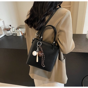 Detail of a black leather bucket bag with baseball charms on a shoulder strap