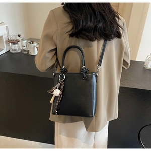 Lifestyle shot of a black minimalist bucket bag with baseball charms and knotted handles