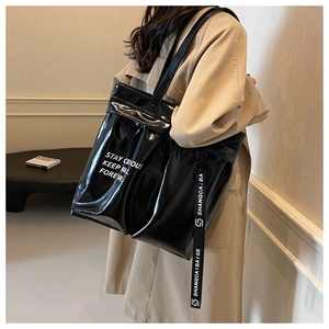 Detail of black glossy tote bag featuring white slogan print and decorative logo ribbon
