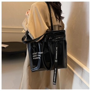 Detail of glossy black patent leather tote bag with white lettering and long decorative strap