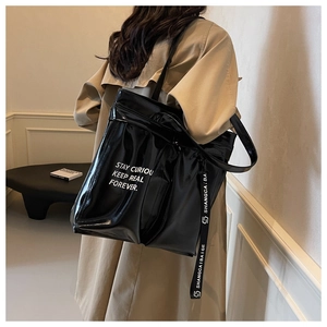 Detail of black patent leather tote bag with white text and hanging brand ribbon
