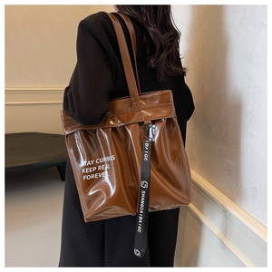 Detail of glossy brown tote bag with white slogan and branding strap over model shoulder