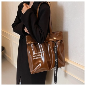 Close-up of brown glossy tote bag with white lettering and black brand ribbon