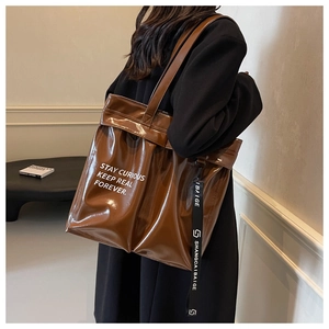 Detail of glossy brown oversized tote bag featuring a white slogan and woven strap pendant