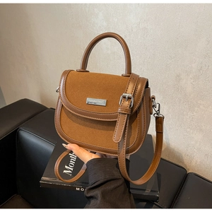 Détail d'un sac besace marron avec textures mixtes et logo argenté sur un canapé noir