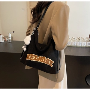 Dettaglio borsa tote grande in tela nera con patch HELNDAY in peluche e ciondolo a pompon