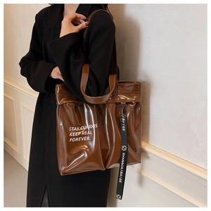 Detailed close-up of brown glossy patent leather tote bag with stylish side ribbon strap