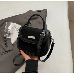 Détail du sac selle noir minimaliste avec logo en métal argenté et texture patchwork en cuir
