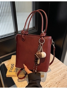 Minimalist deep red bucket tote bag with knot handles and baseball charm on marble surface