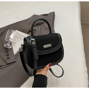 Détail du sac selle noir mat avec plaque de marque argentée et bordures en cuir fin