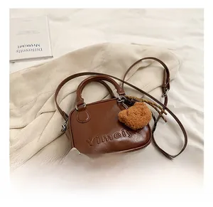 Detail of dark brown faux leather handbag with embossed letters and plush bear charm