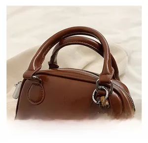 Detail of a dark brown PU leather handbag featuring dual handles and a cute plush bear charm