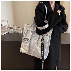 Detail of silver metallic tote bag featuring black STAY CURUS text and woven strap