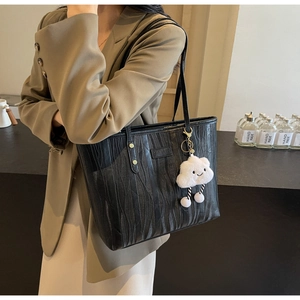 Détail du sac cabas noir avec texture ondulée, logo en métal et breloque nuage en peluche