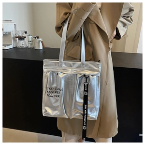 Close-up of metallic silver tote bag featuring industrial text and black accent strap