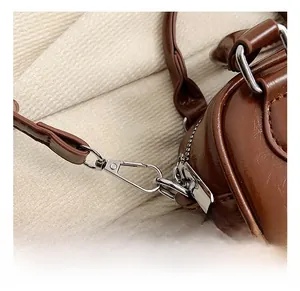 Detail of silver lobster swivel clasp and D-ring on brown leather crossbody bag