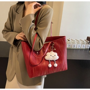 Détail du cabas rouge foncé avec texture grain de bois et breloque nuage en peluche sur l'épaule
