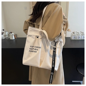 Detail view of large white PU leather tote bag with black typography on casual trench coat