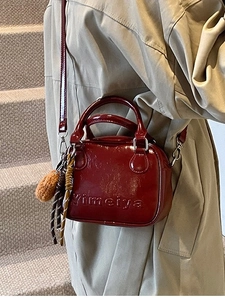 Burgundy patent leather mini crossbody bag with bear charm and brand logo on beige coat