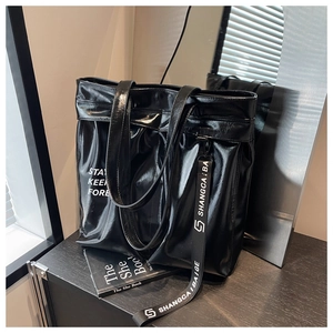 Macro detail of glossy black faux leather tote bag with white lettering and side strap